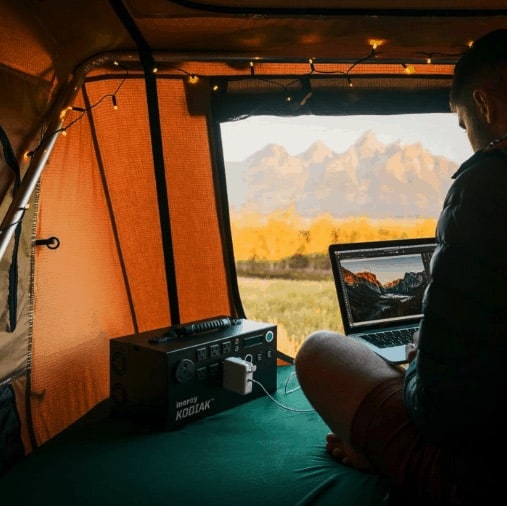 Person using laptop with Inergy Kodiak generator in tent