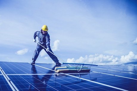 man cleaning solar panels on roof